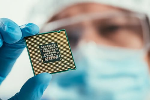 Close-up of a gloved hand holding a semiconductor chip for inspection in a cleanroom environment.